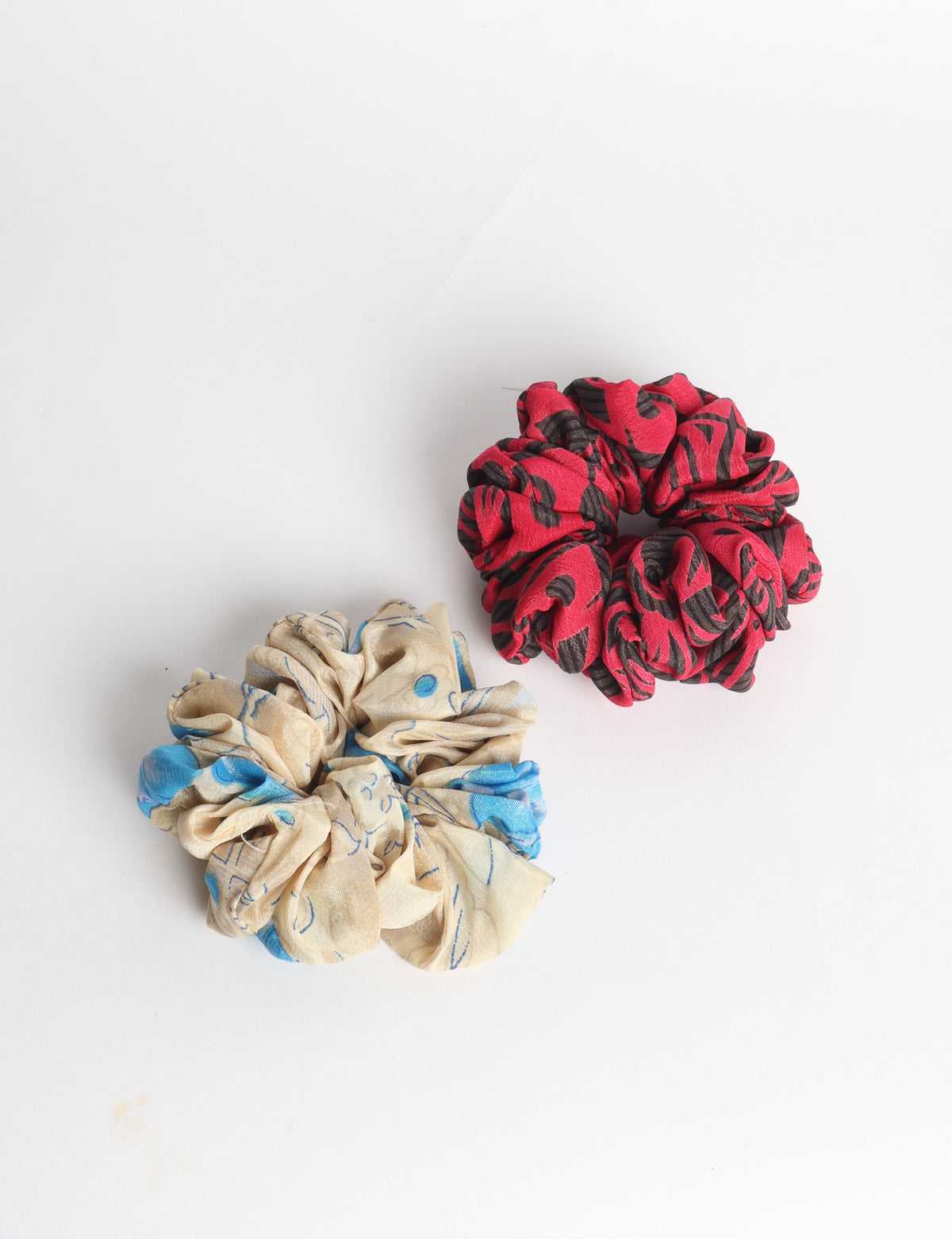 Set of two fabric scrunchies, one turquoise with beige abstract spots, one red with white linear pattern, flat lay on white
