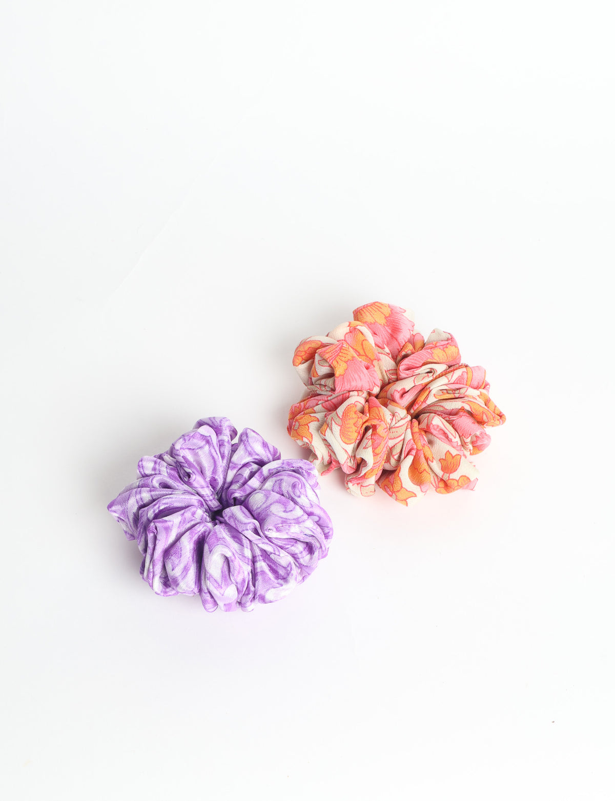 Set of two fabric scrunchies, one turquoise with beige abstract spots, one red with white linear pattern, flat lay on white