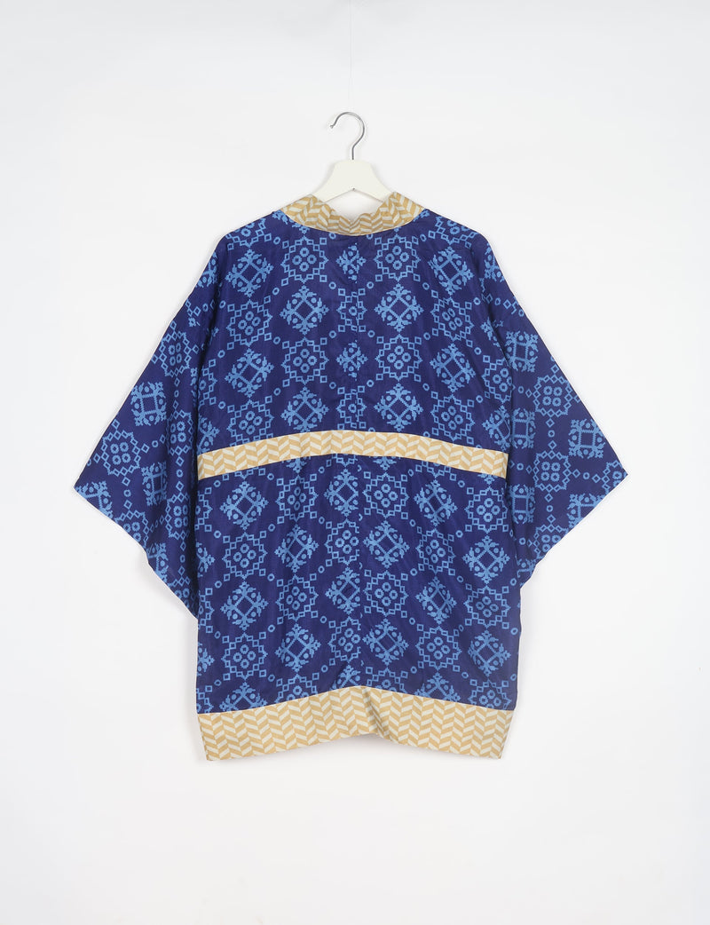 Blue kimono with light blue geometric patterns and beige chevron trim on collar, waist, and hem, shown from back on hanger