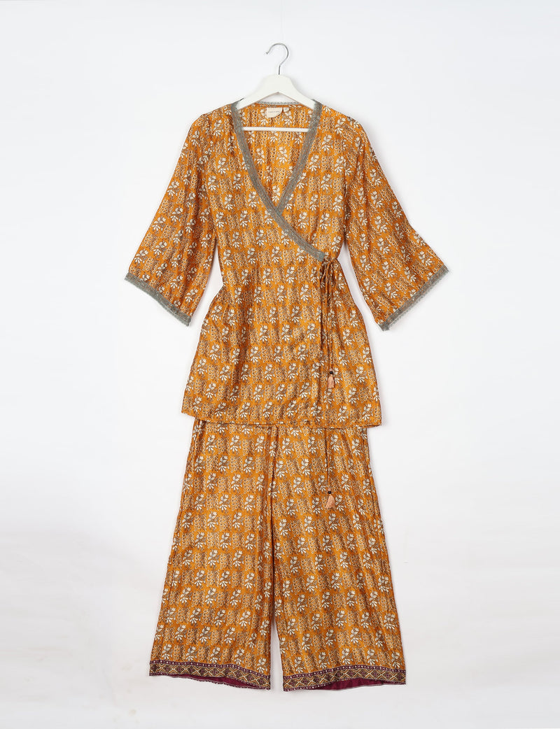 Yellow floral print tunic and pants set with gray lace trim on sleeves and neckline, hanging on white hanger, front view
