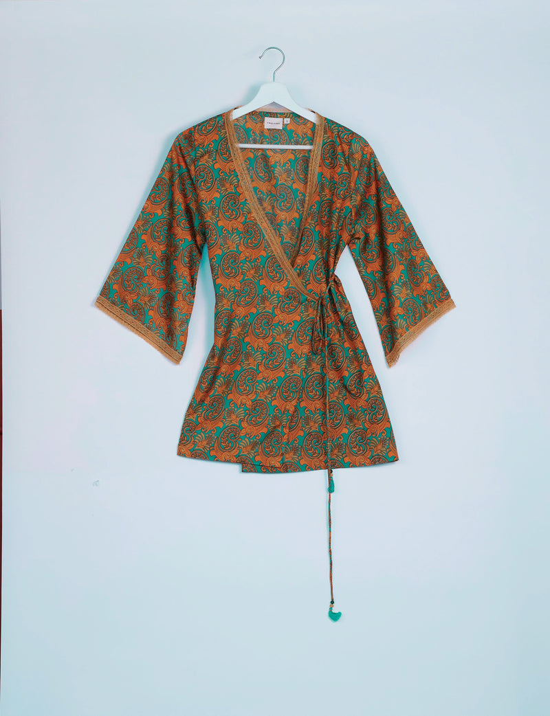 Green paisley wrap tunic with orange and brown floral patterns, lace trim on neckline and sleeves, hanging on white hanger