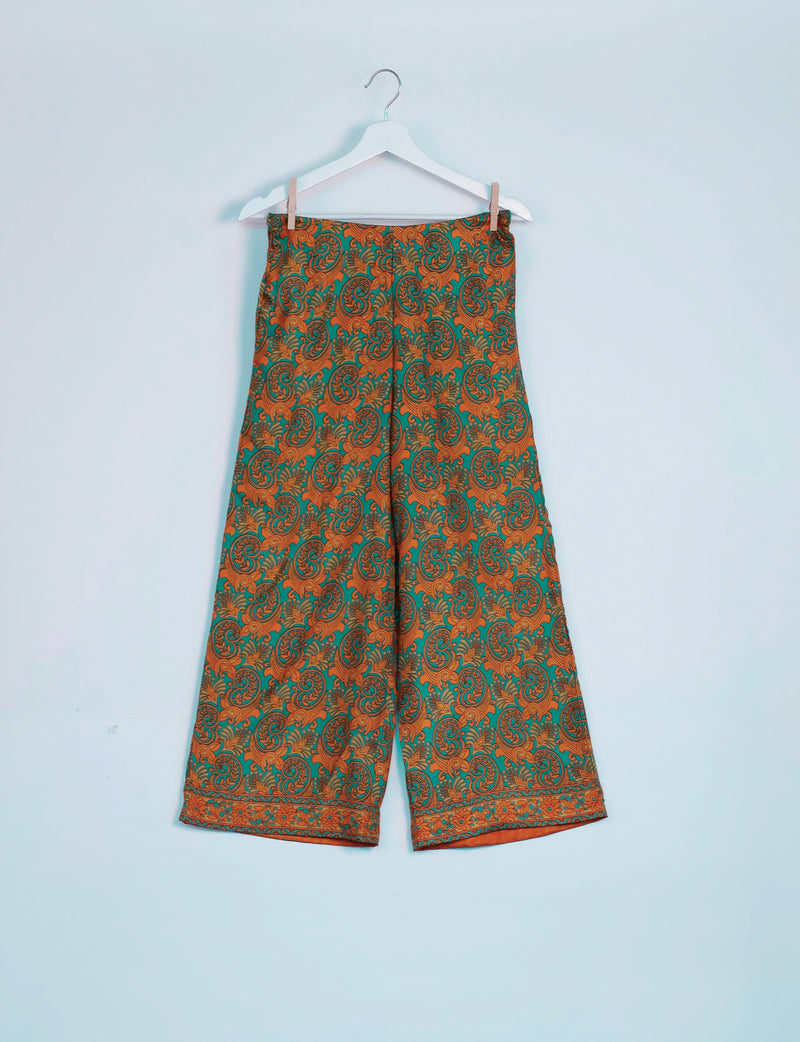 Green and orange paisley patterned wide-leg pants hanging on a white hanger against a light blue background