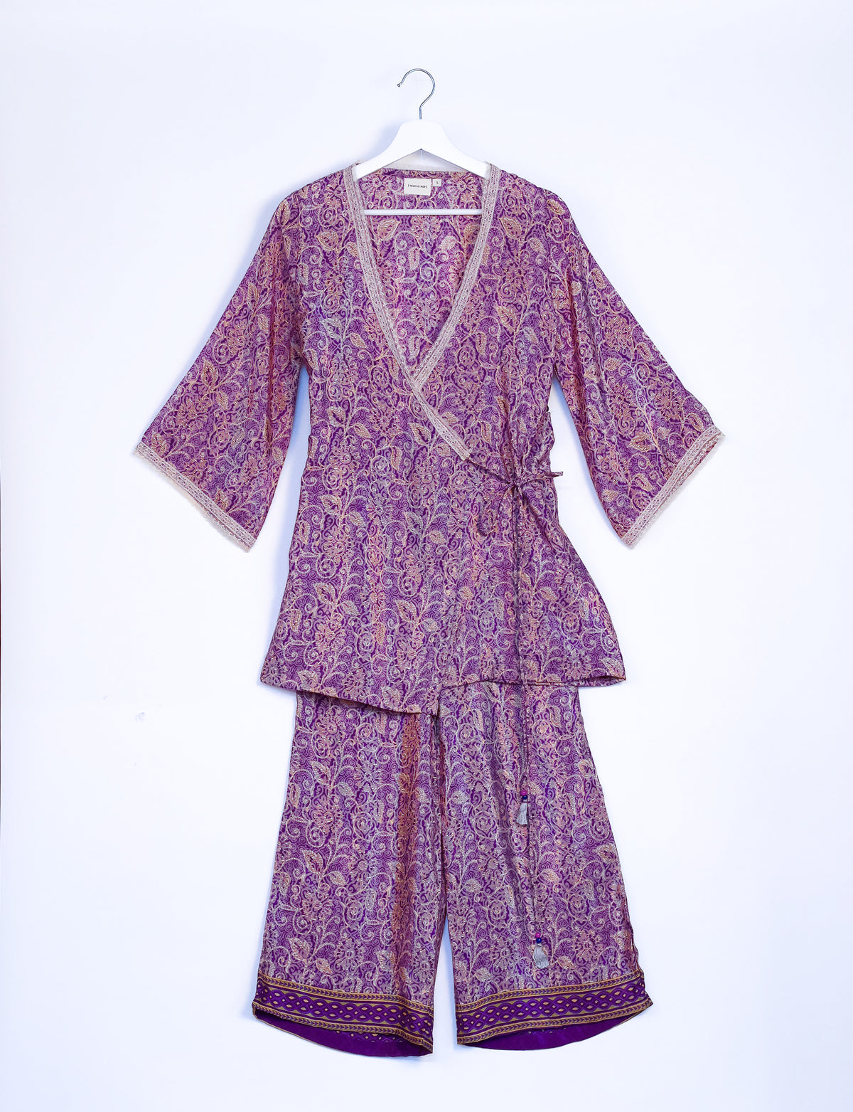 Purple tropical print tunic set with wrap front, three-quarter sleeves, and decorative border on pants, hanging on white hanger