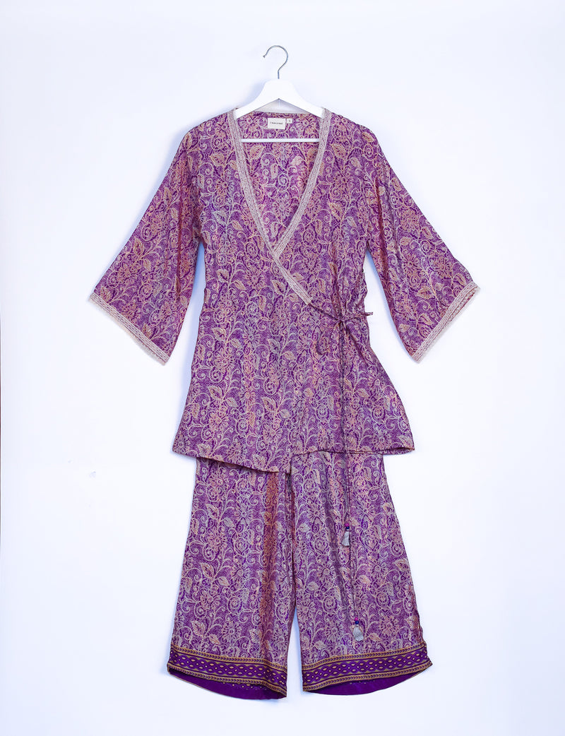 Purple tropical print tunic set with wrap front, three-quarter sleeves, and decorative border on pants, hanging on white hanger