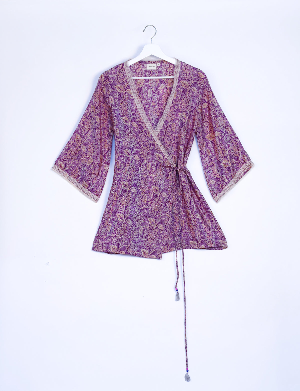 Purple tropical print wrap tunic with beige lace trim on neckline and sleeves, hanging on white hanger front view