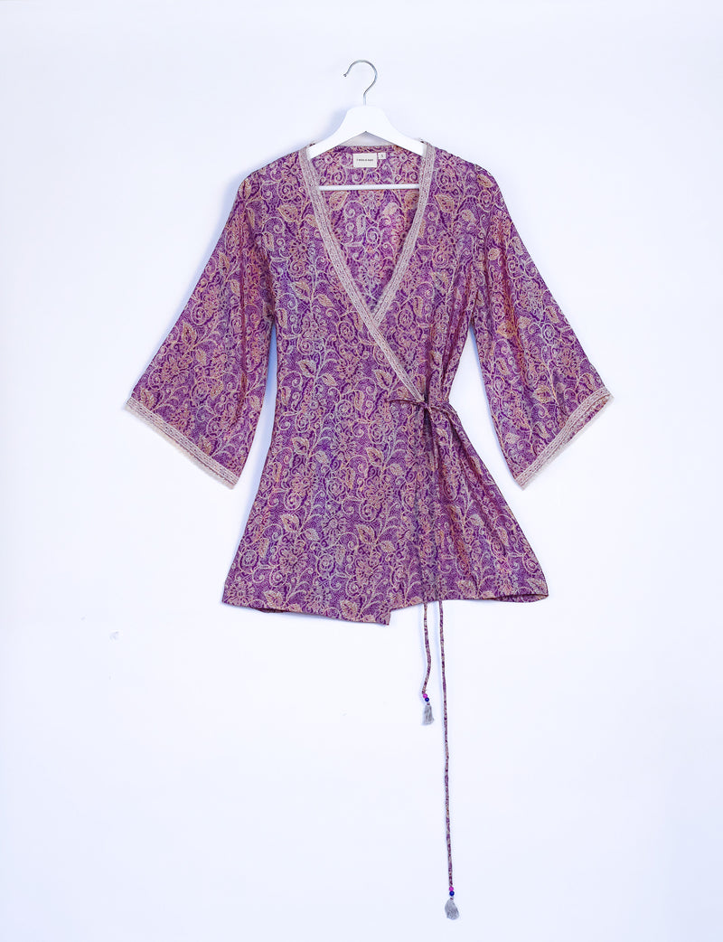 Purple tropical print wrap tunic with beige lace trim on neckline and sleeves, hanging on white hanger front view