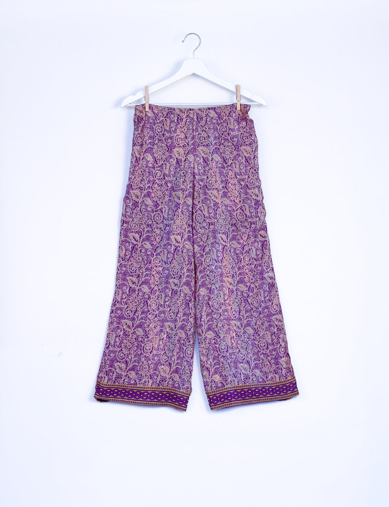 Purple tropical patterned wide-leg pants with elastic waistband and decorative border hem, hanging on white hanger