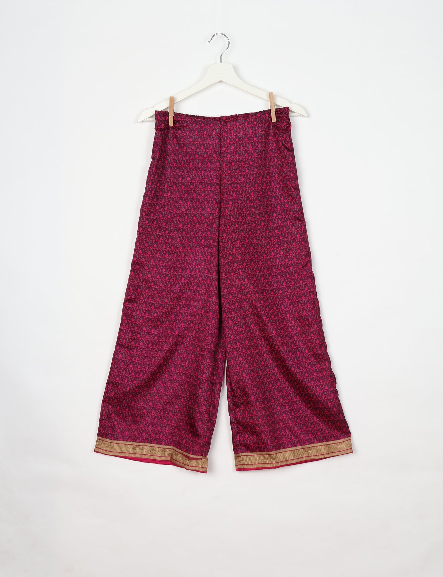 Pink tunic pants with dark micro floral pattern and gold border hem, hanging on white hanger against white background