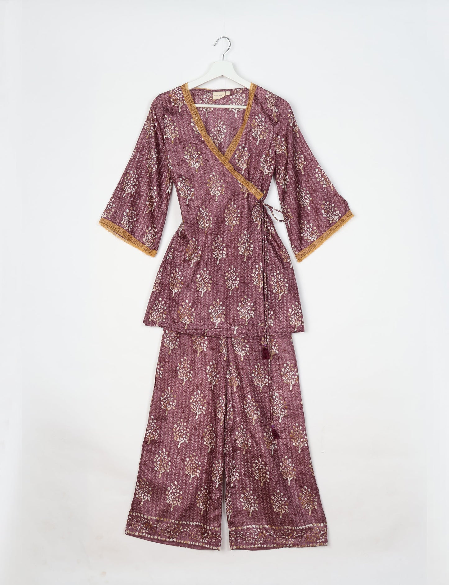 Purple tropical print tunic set with wrap top featuring mustard lace trim and matching wide-leg pants, flat lay on hanger