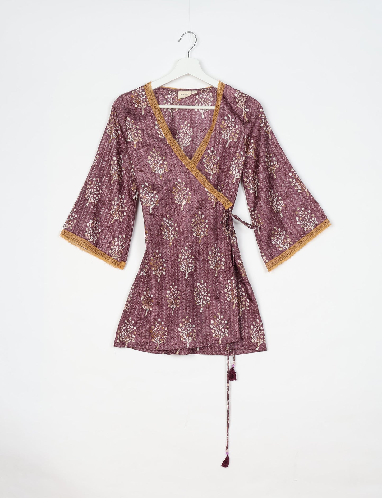 Purple wrap tunic with white and gold tropical print, lace trim on neckline and sleeves, hanging on white hanger