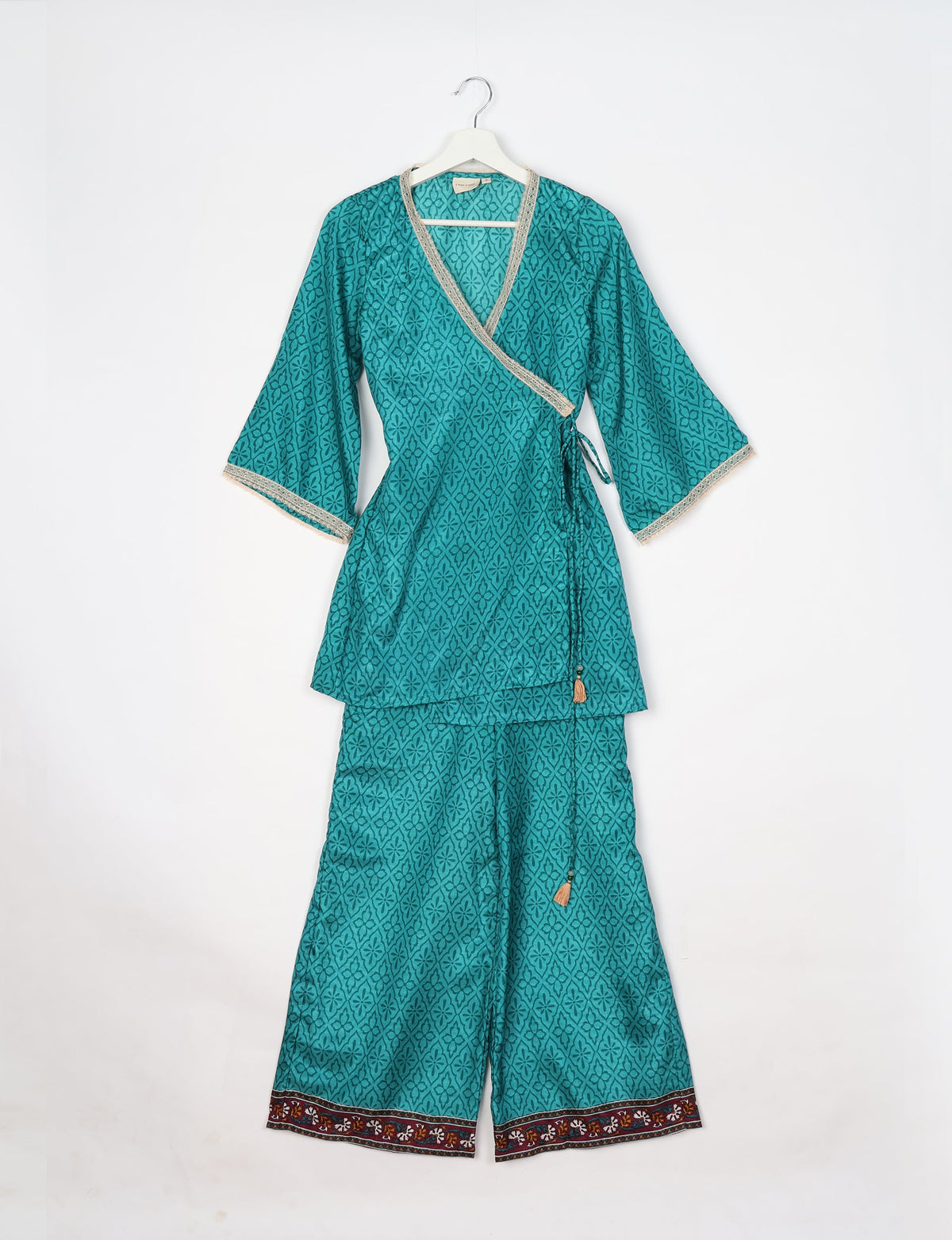 Blue abstract patterned tunic set with wrap top, lace trim, and wide-leg pants with floral border, hanging on white hanger
