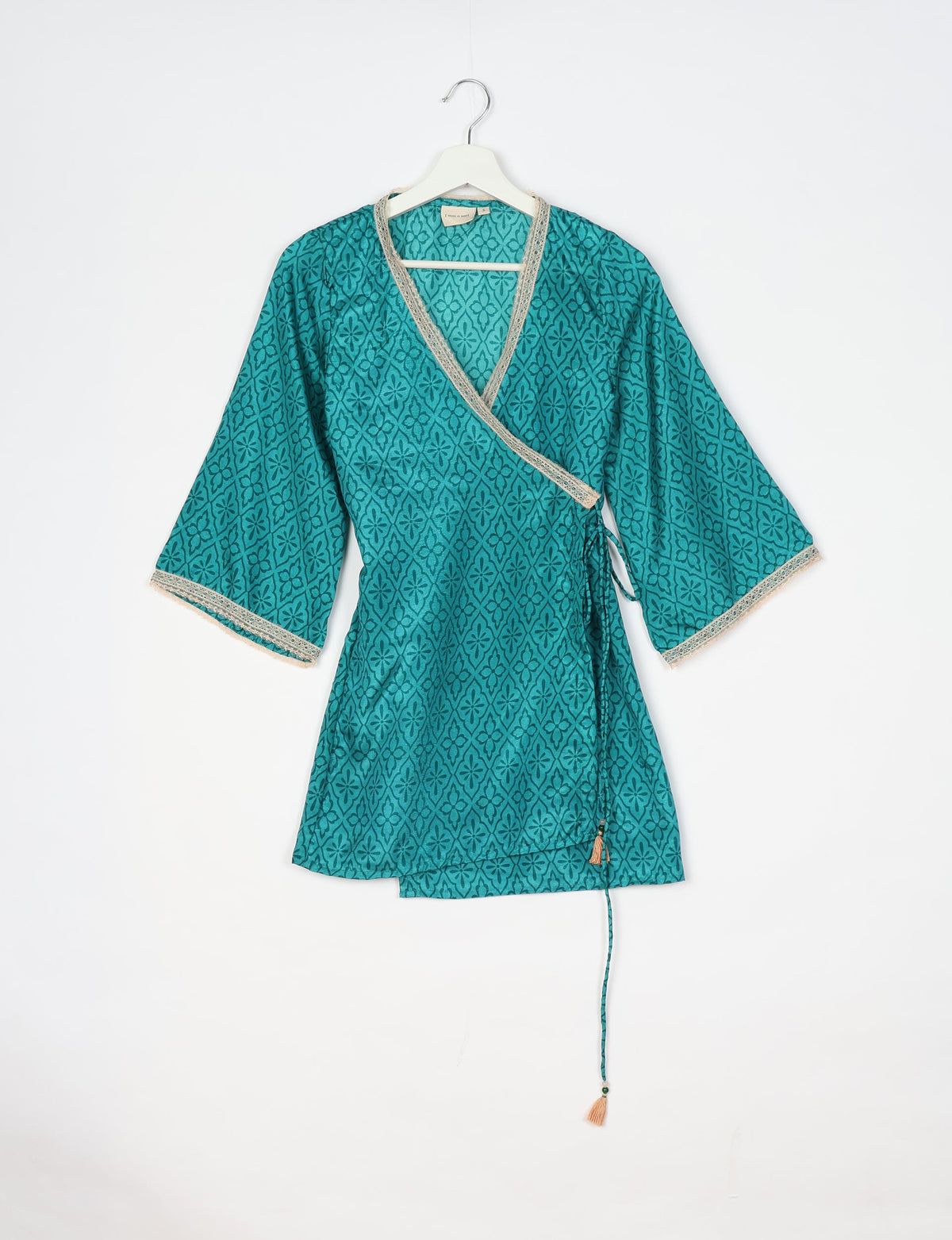 Blue abstract patterned tunic with wrap style, V-neckline, wide sleeves, and beige lace trim, hanging on a white hanger