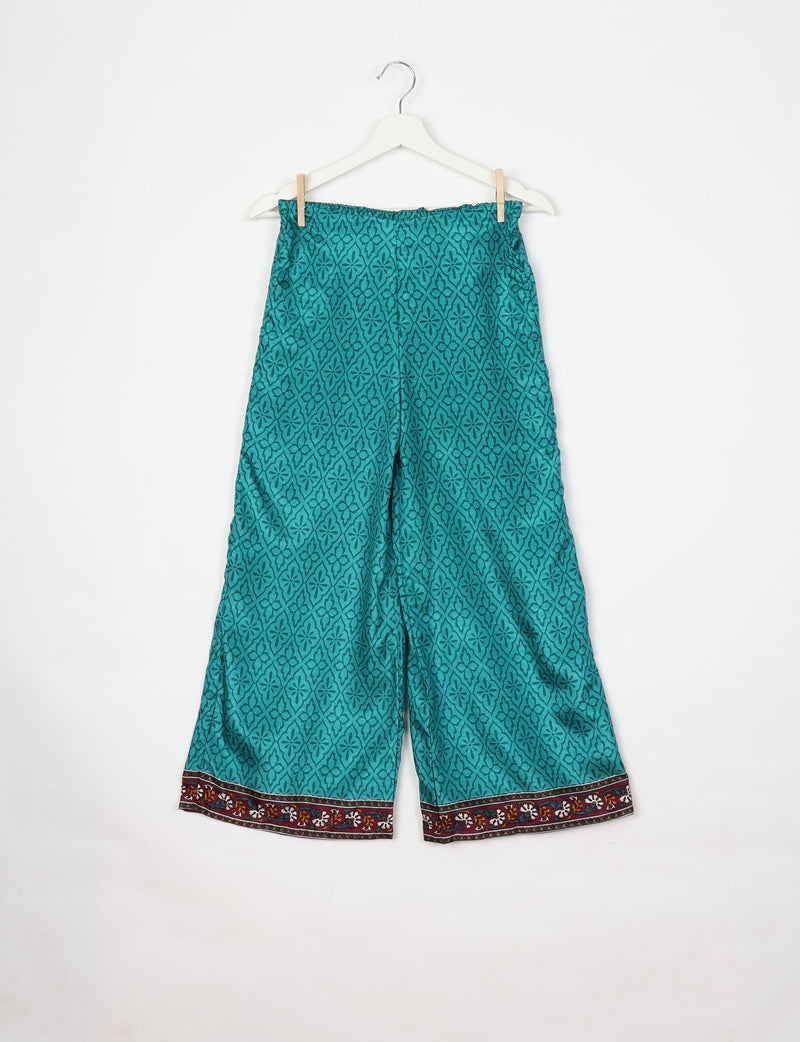 Blue patterned tunic pants with elastic waistband and floral border hem, hanging on white hanger against white background