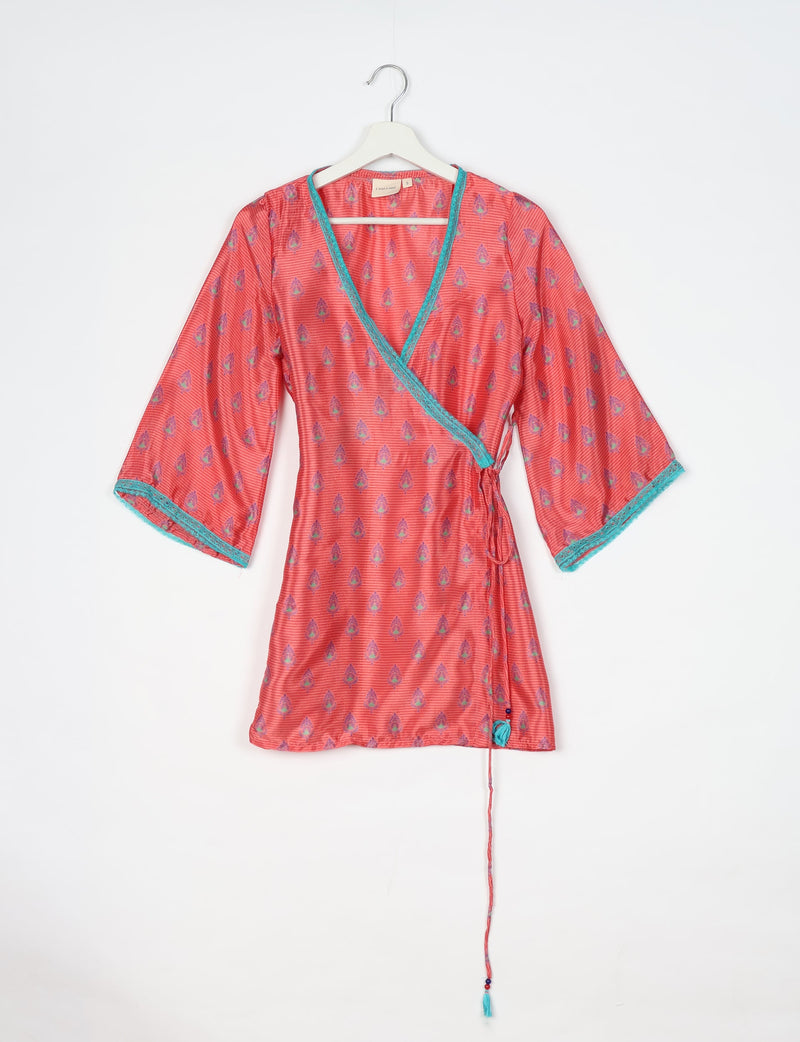 Pink tunic with micro floral design, turquoise trim, wrap style, and three-quarter sleeves hanging on white hanger