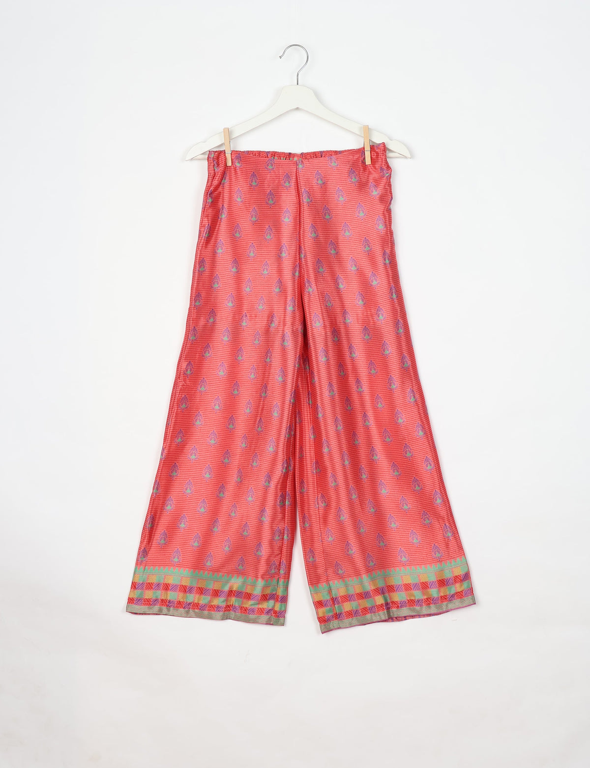 Pink wide-leg pants with purple micro design and multicolor checkered border, hanging on white hanger with clips