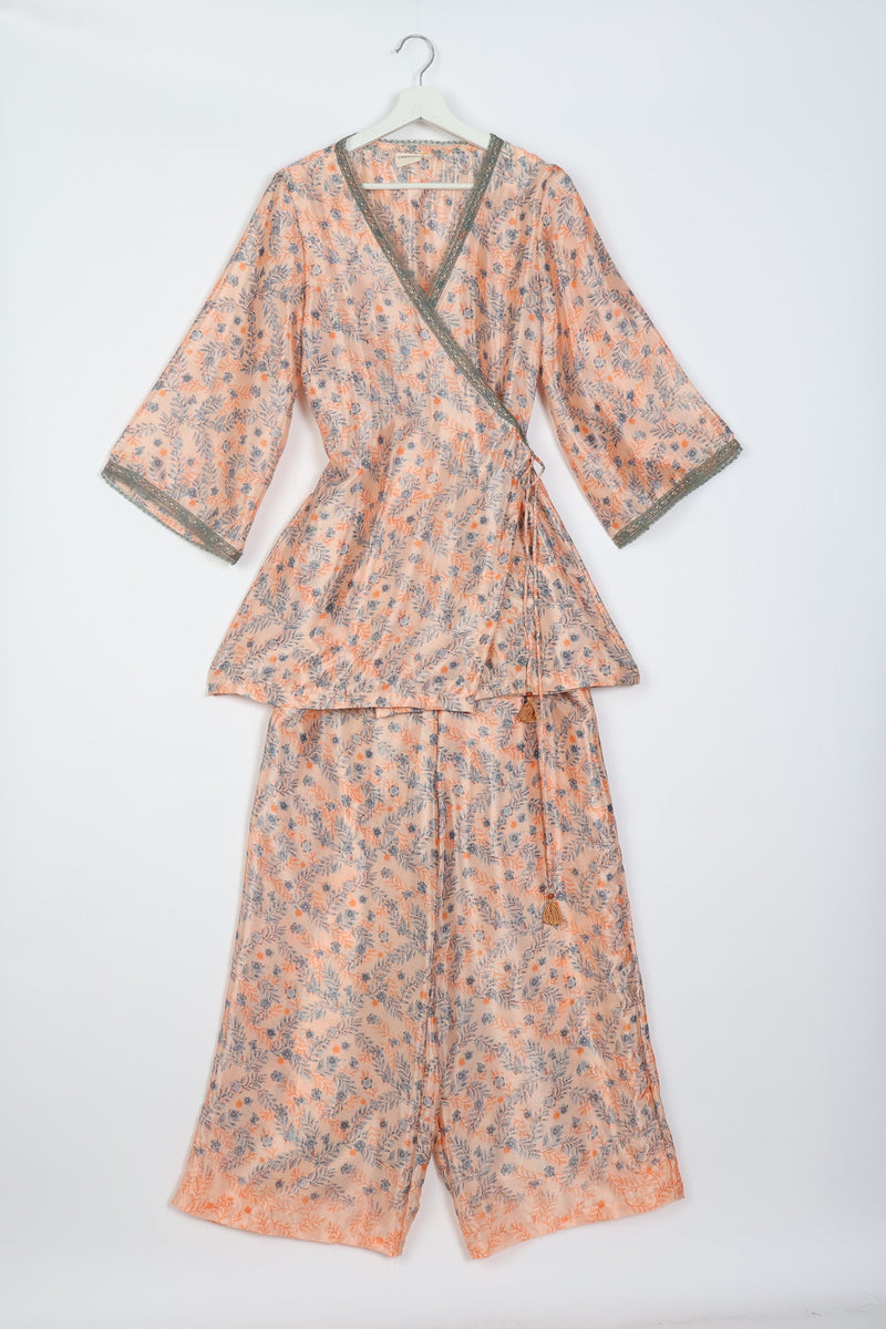 Pink floral print tunic set with wrap front, three-quarter sleeves, green lace trim, and matching wide-leg pants on hanger