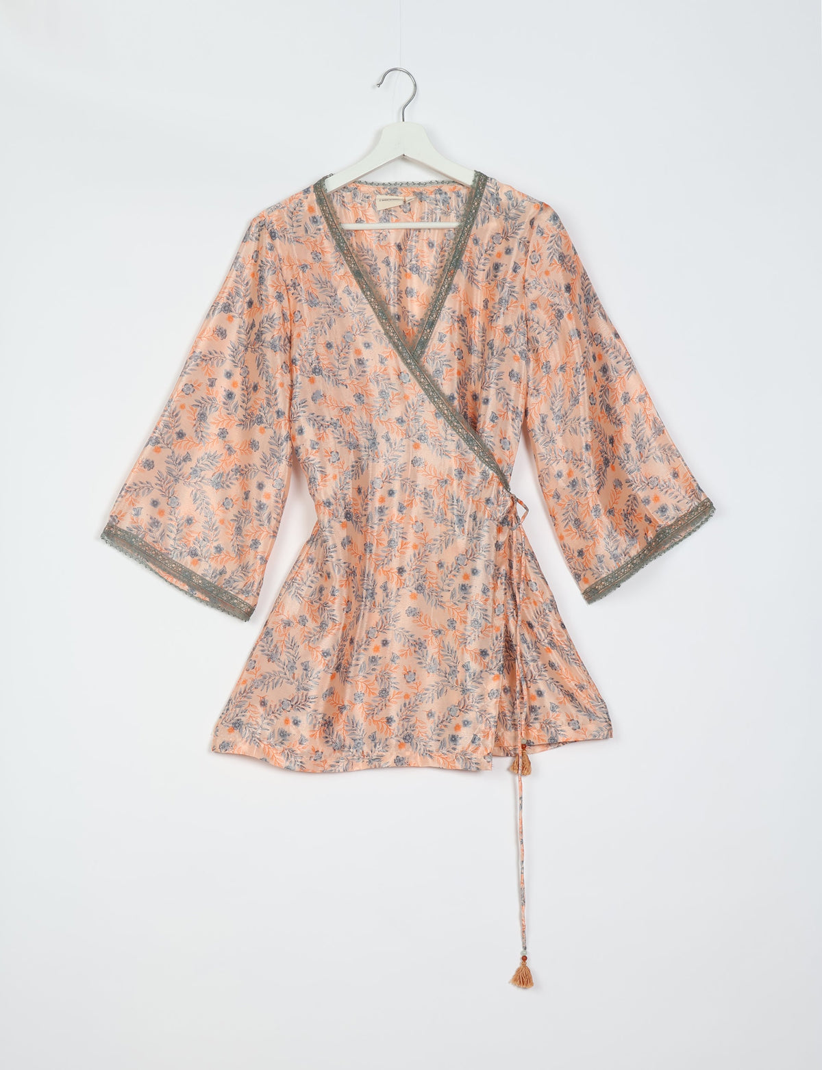 Pink floral wrap tunic with gray lace trim on neckline and sleeves, hanging on white hanger against white background