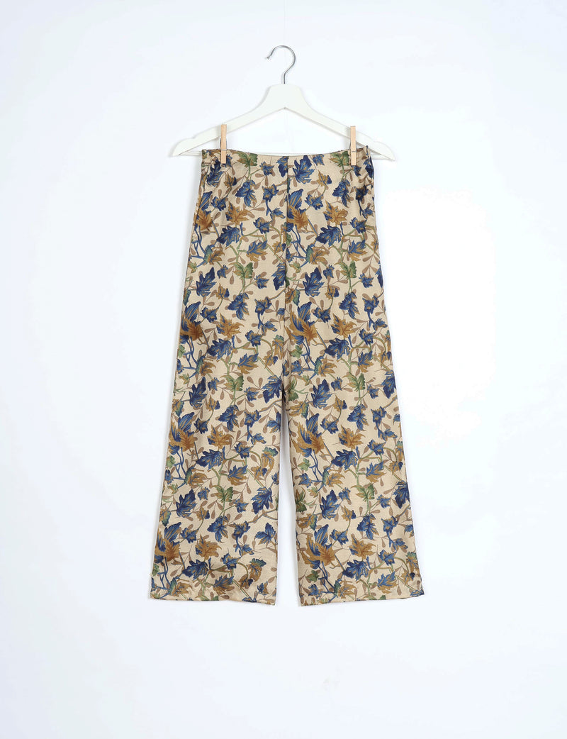 Beige tunic pants with blue, green, and brown leaf print hanging on white hanger against white background