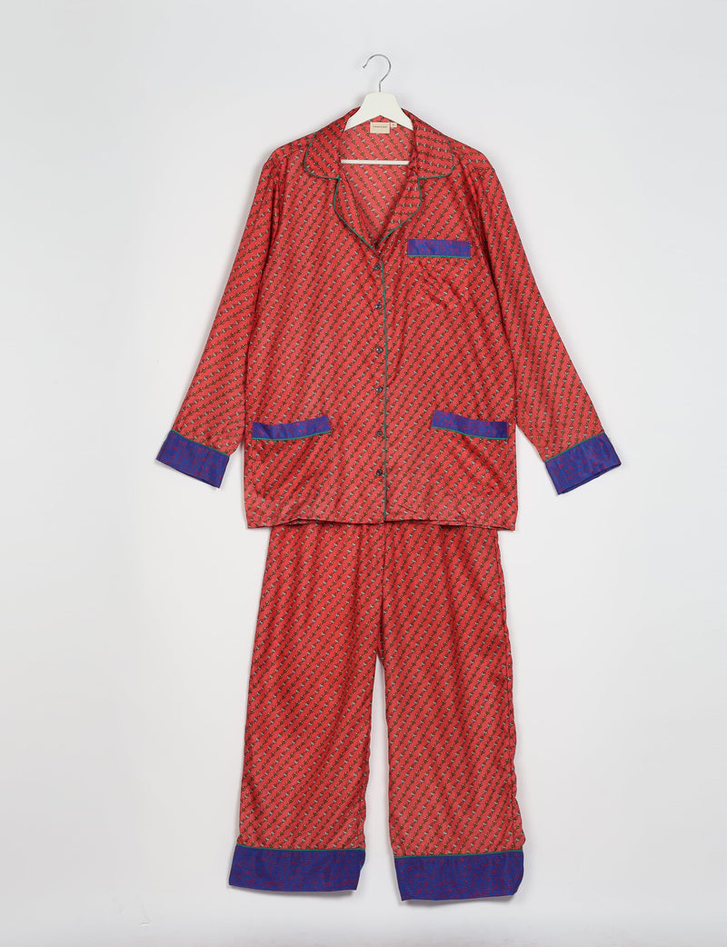 Orange long-sleeve pajama set with micro floral design and blue contrast cuffs and pocket trim, hanging flat on a white background