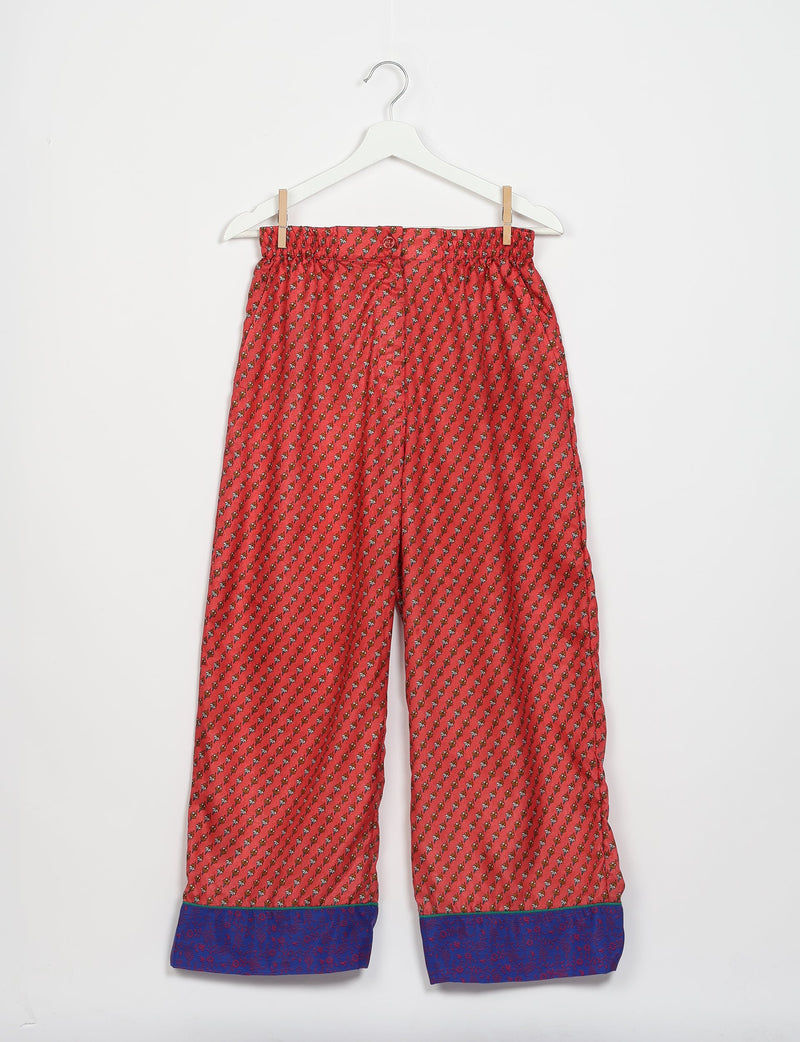 Red pajama pants with small floral micro design and blue floral cuffs hanging on white hanger against white background