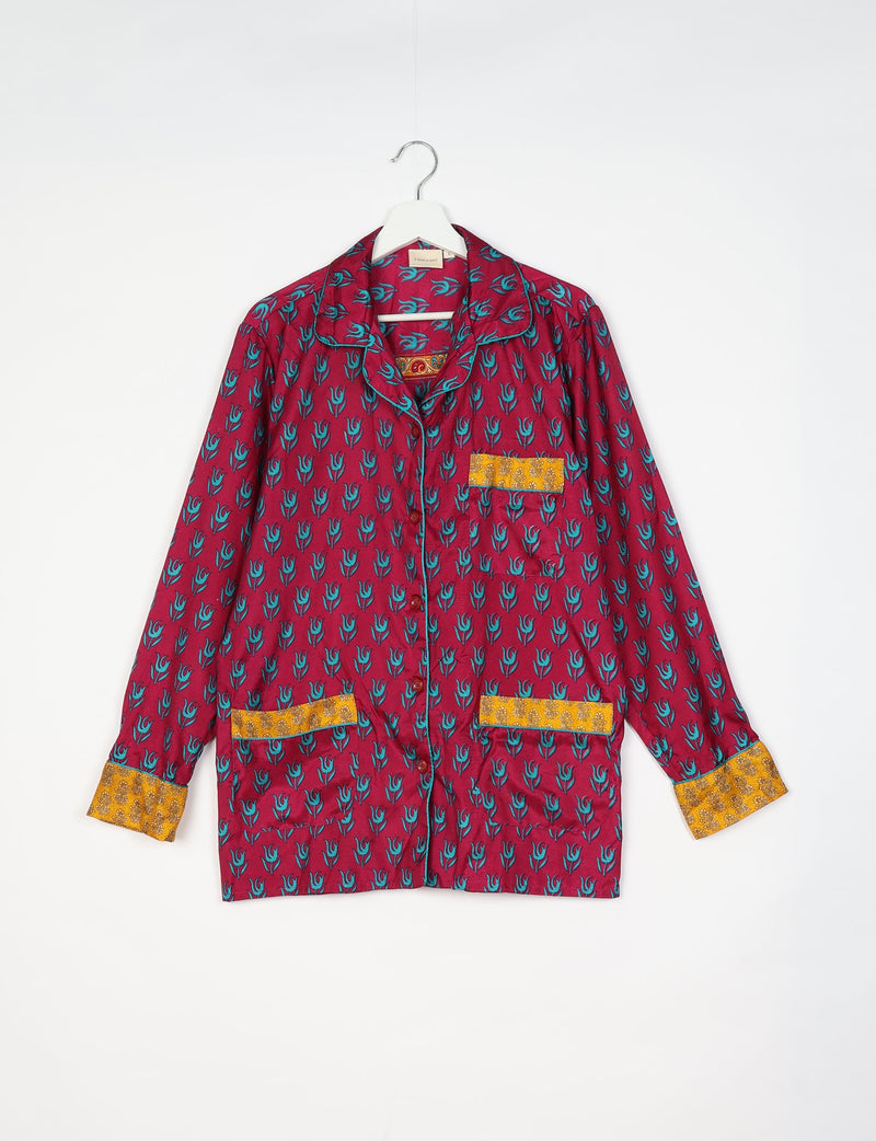 Long-sleeve red pajama top with blue tropical print and yellow patterned cuffs and pockets, hanging on white hanger
