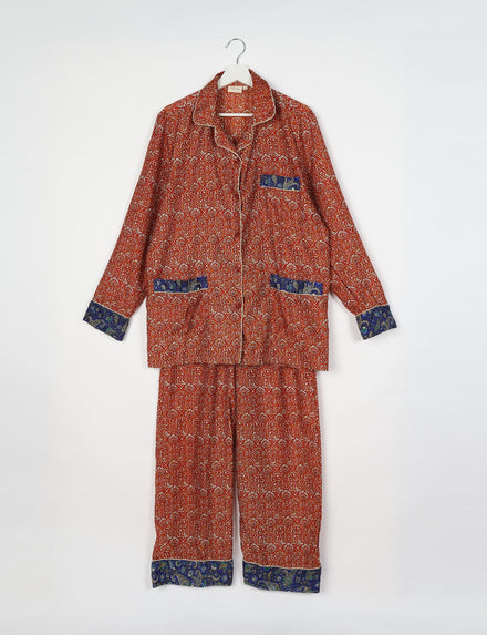 Long-sleeve pajama set with red geometric and floral print, blue paisley trim on cuffs, pockets, and pant hems, hanging flat