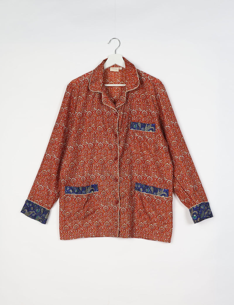 Long-sleeve red pajama top with geometric and floral patterns, blue paisley trim on cuffs and pockets, hanging on white hanger