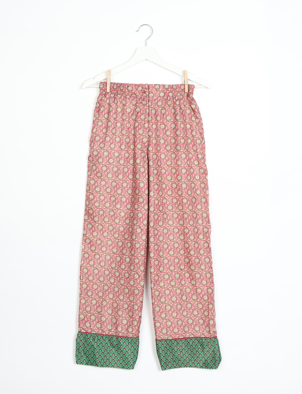 Pink patterned pajama pants with green patterned cuffs hanging on a white hanger against a white background