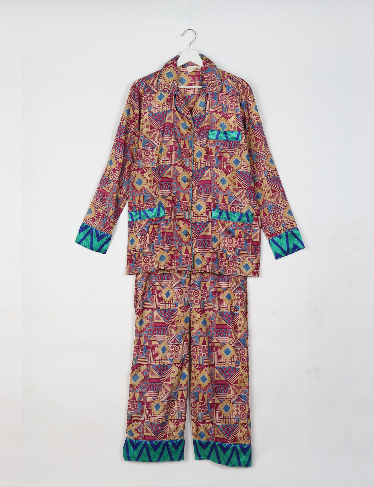 Pink geometric long-sleeve pajama set with blue and green chevron cuffs, front pockets, and button closure, hanging on a white hanger