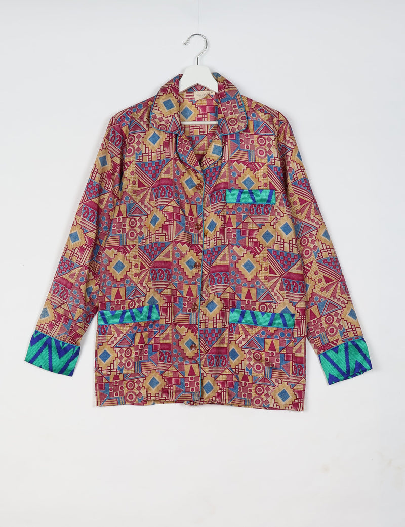 Long-sleeve button-up shirt with red, blue, and tan geometric pattern and green-blue chevron cuffs and pocket accents hanging on white hanger