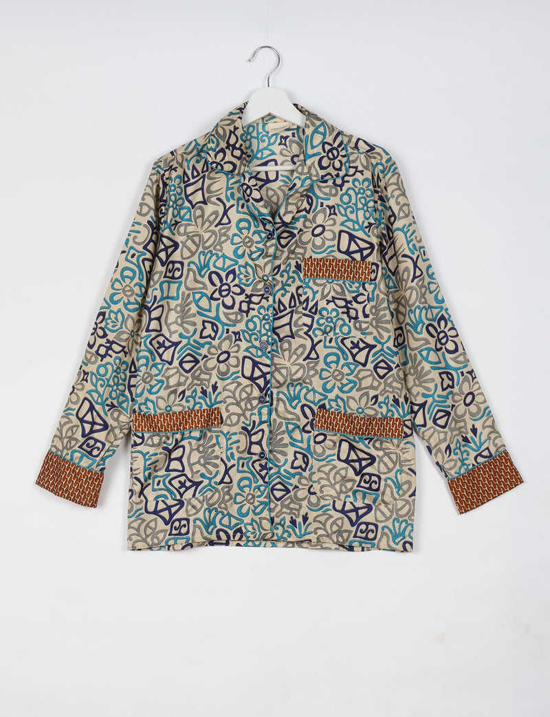 Beige long-sleeve pajama top with blue and gray abstract floral print, brown patterned cuffs and pocket trims, front buttons