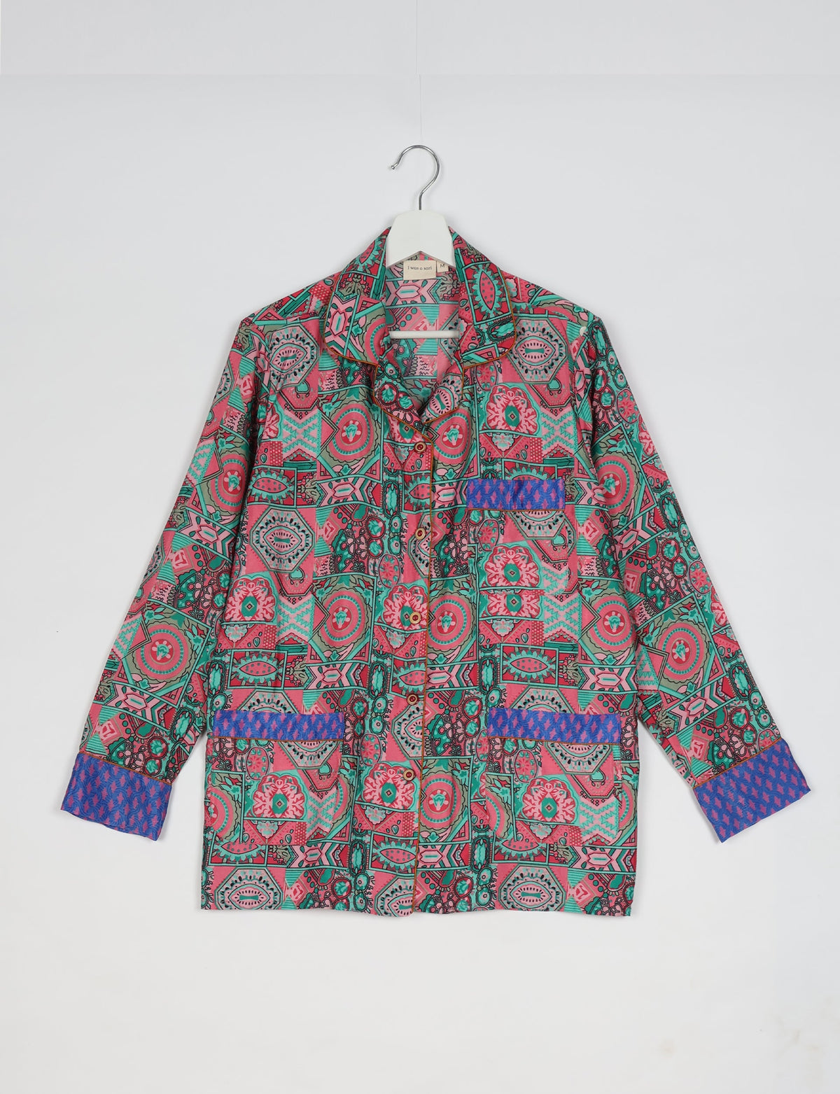 Pink and green Indian ethnic patterned long-sleeve pajama top with blue patterned cuffs and pocket accents hanging on white hanger