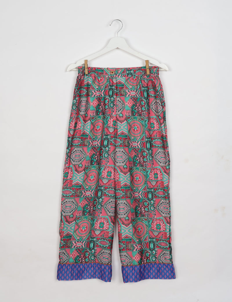 Pink ethnic patterned pajama pants with blue patterned cuffs, hanging on a white hanger against a white background