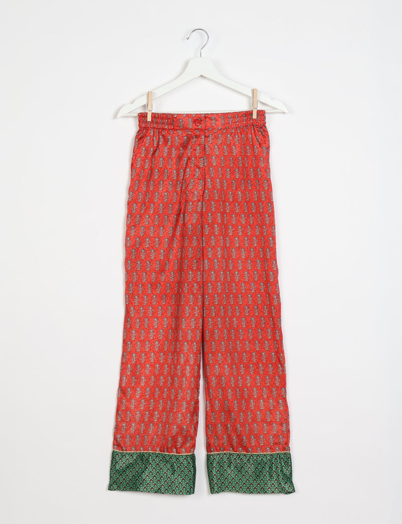 Orange pajama pants with small floral print and green patterned cuffs hanging on white hanger against white background