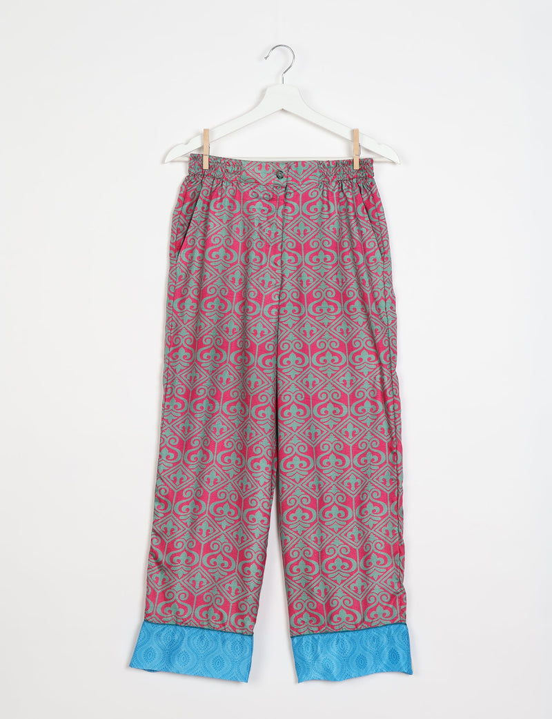 Pink and teal Indian ethnic patterned pajama pants with elastic waistband and blue cuff detail, hanging on white hanger