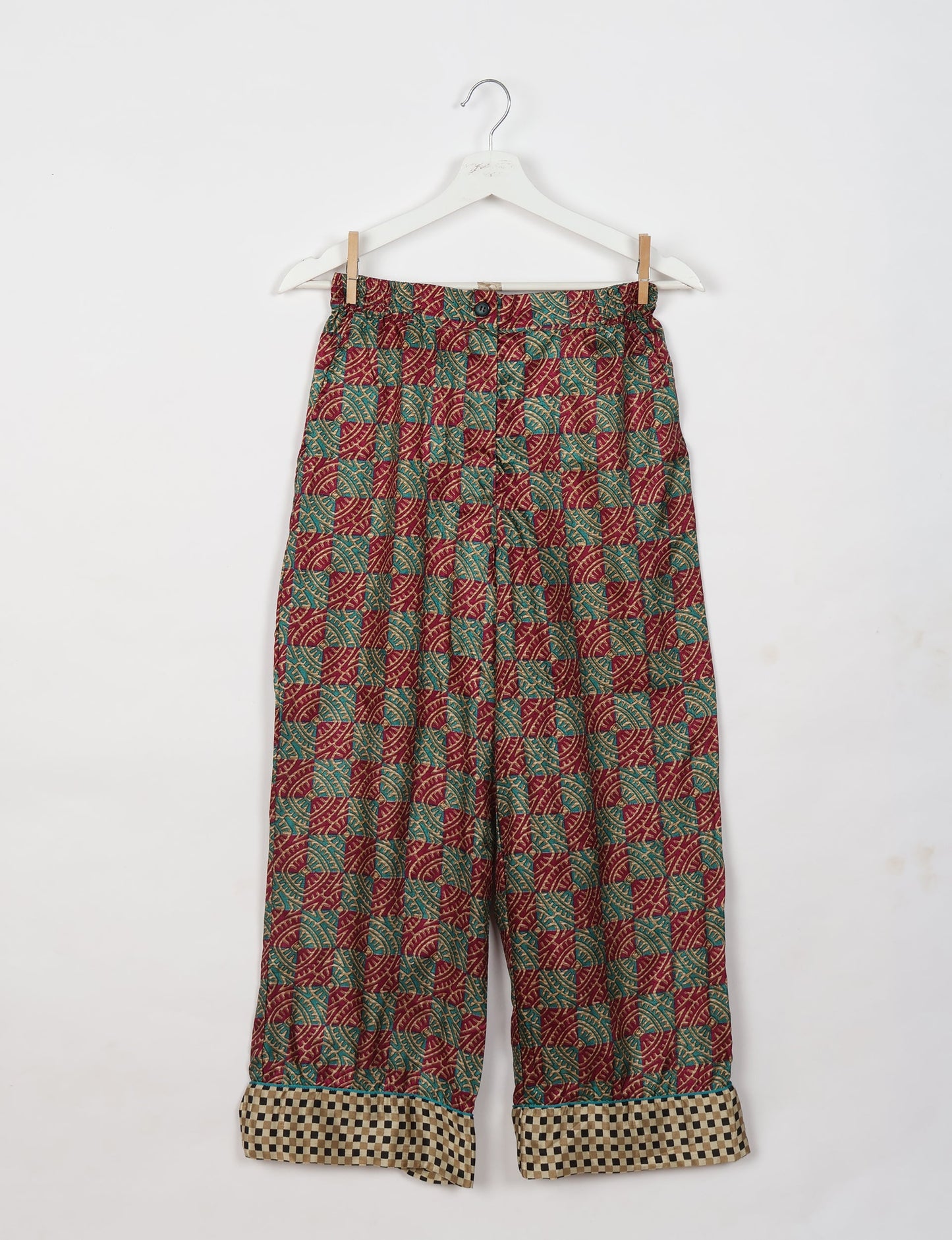 Red tropical patterned pajama pants with button and checkered cuffs, hanging on a white hanger