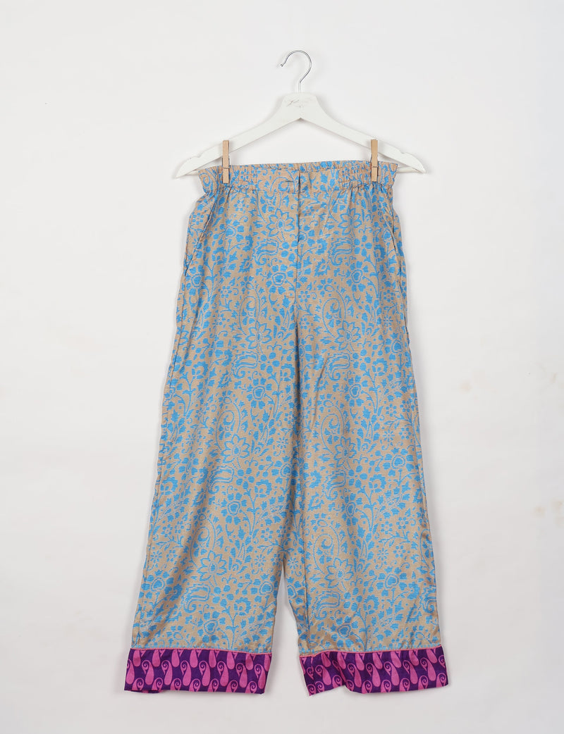 Blue and beige floral patterned pants with purple and pink patterned cuffs hanging on a white hanger against a white background