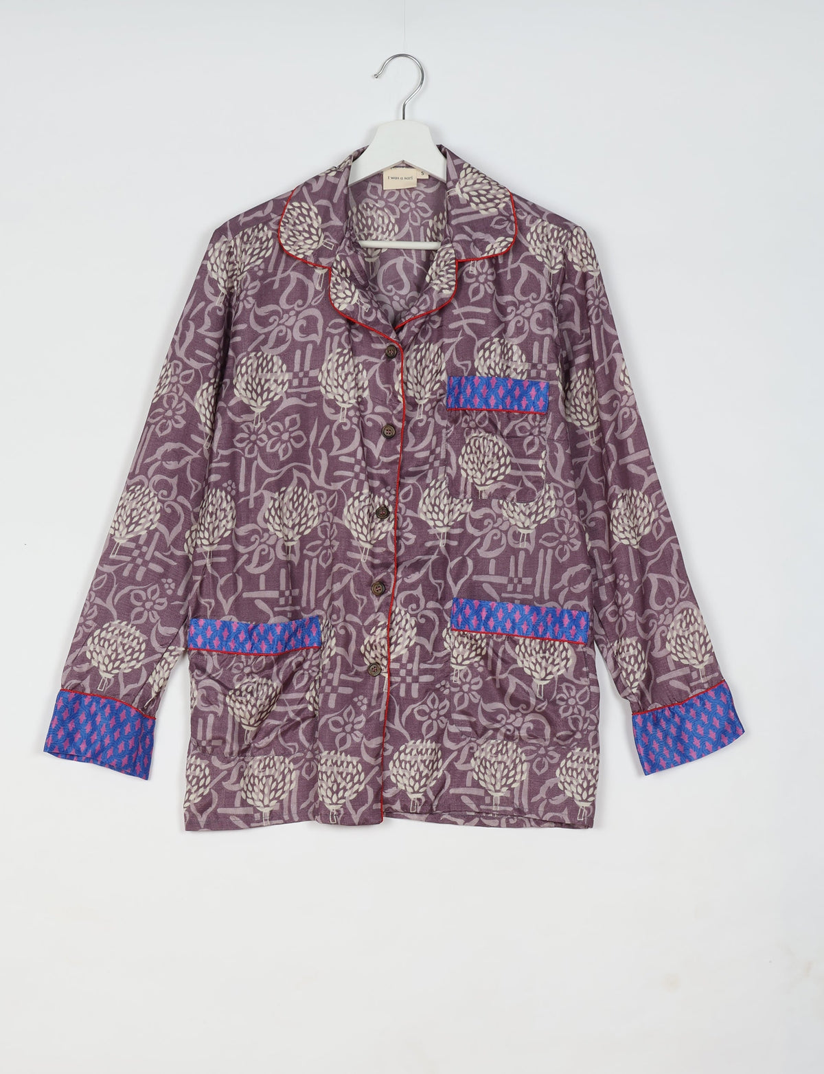 Purple floral long-sleeve pajama top with blue patterned pocket and cuff accents, red piping, and button front, hanging on white hanger
