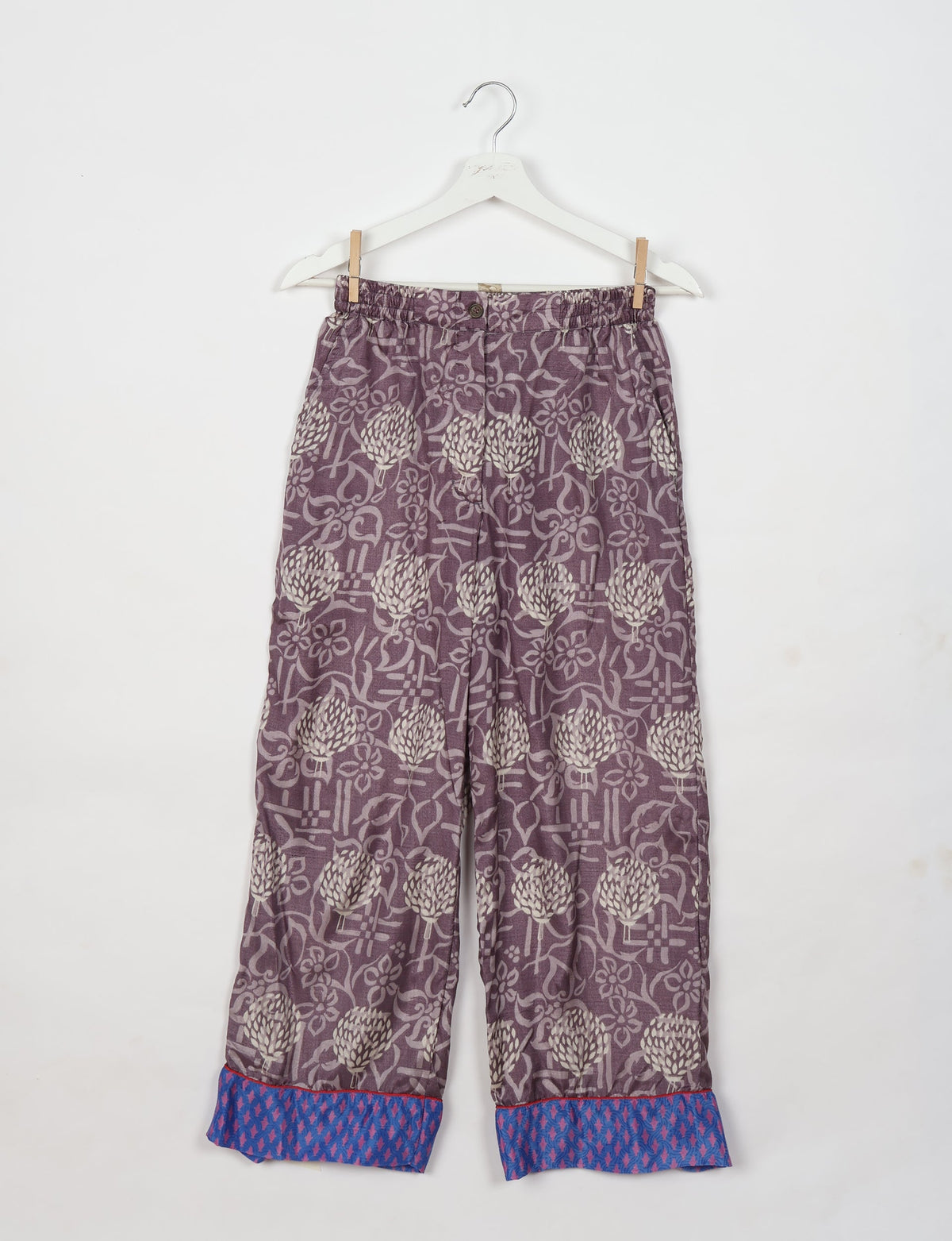 Purple floral pajama pants with blue patterned cuffs, elastic waistband, and button front, hanging on white hanger