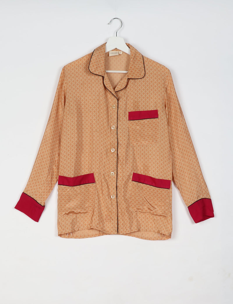 Beige long-sleeve pajama top with micro circular pattern, red pocket and cuff accents, black piping, hanging on white hanger