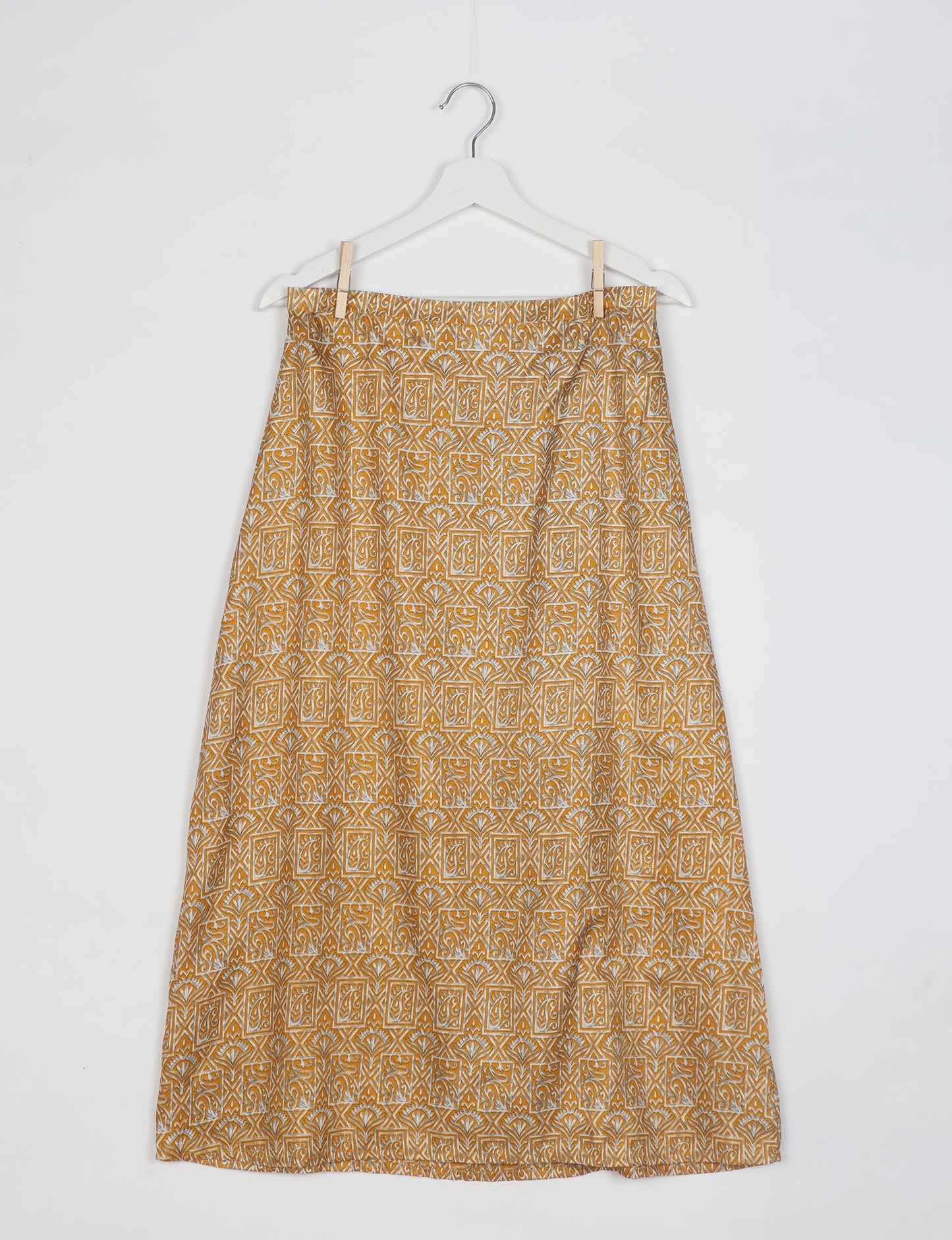 Yellow A-line skirt with white geometric and floral block print pattern, hanging on white hanger against white background