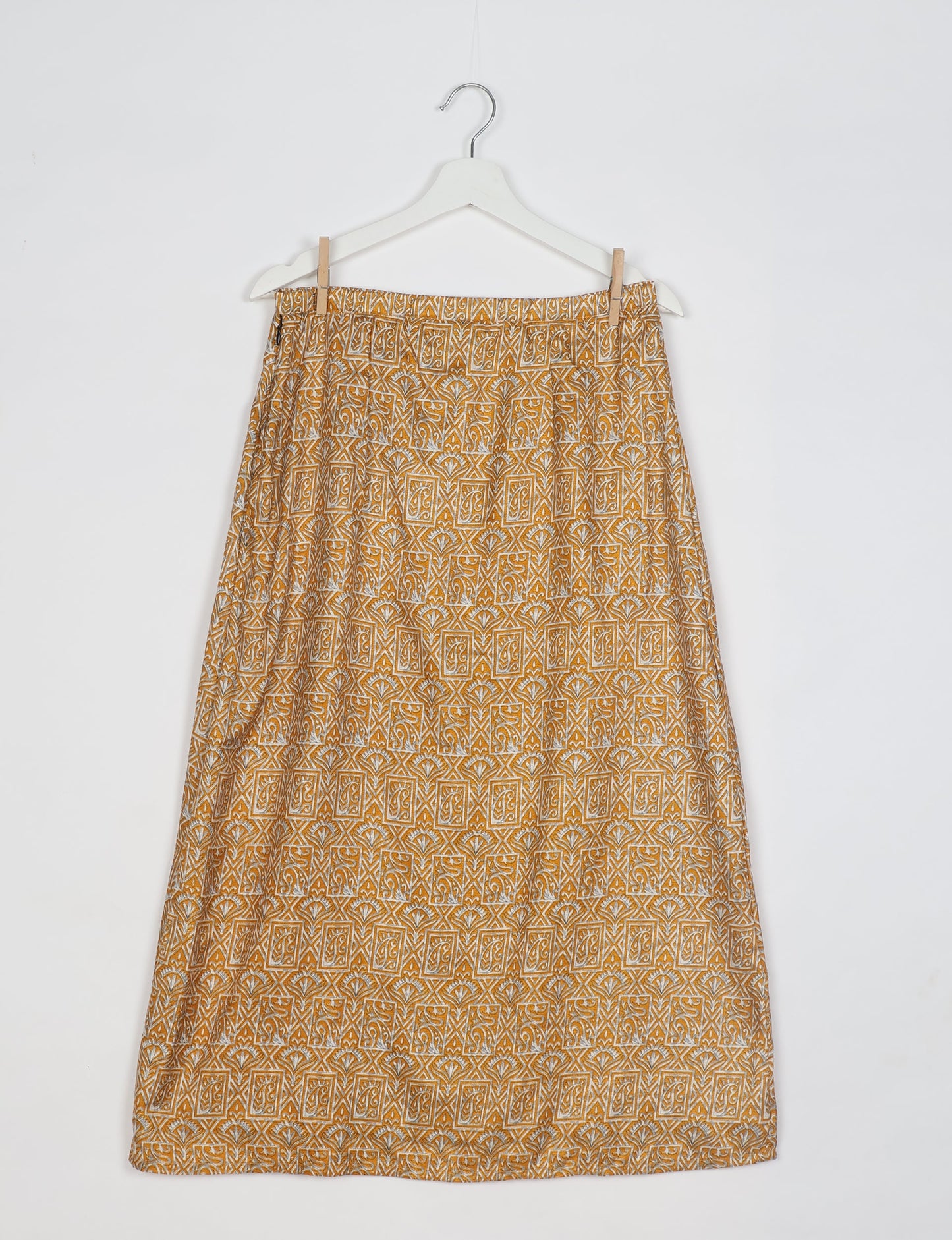 Yellow A-line skirt with white and brown tropical geometric print, hanging on white hanger against white background