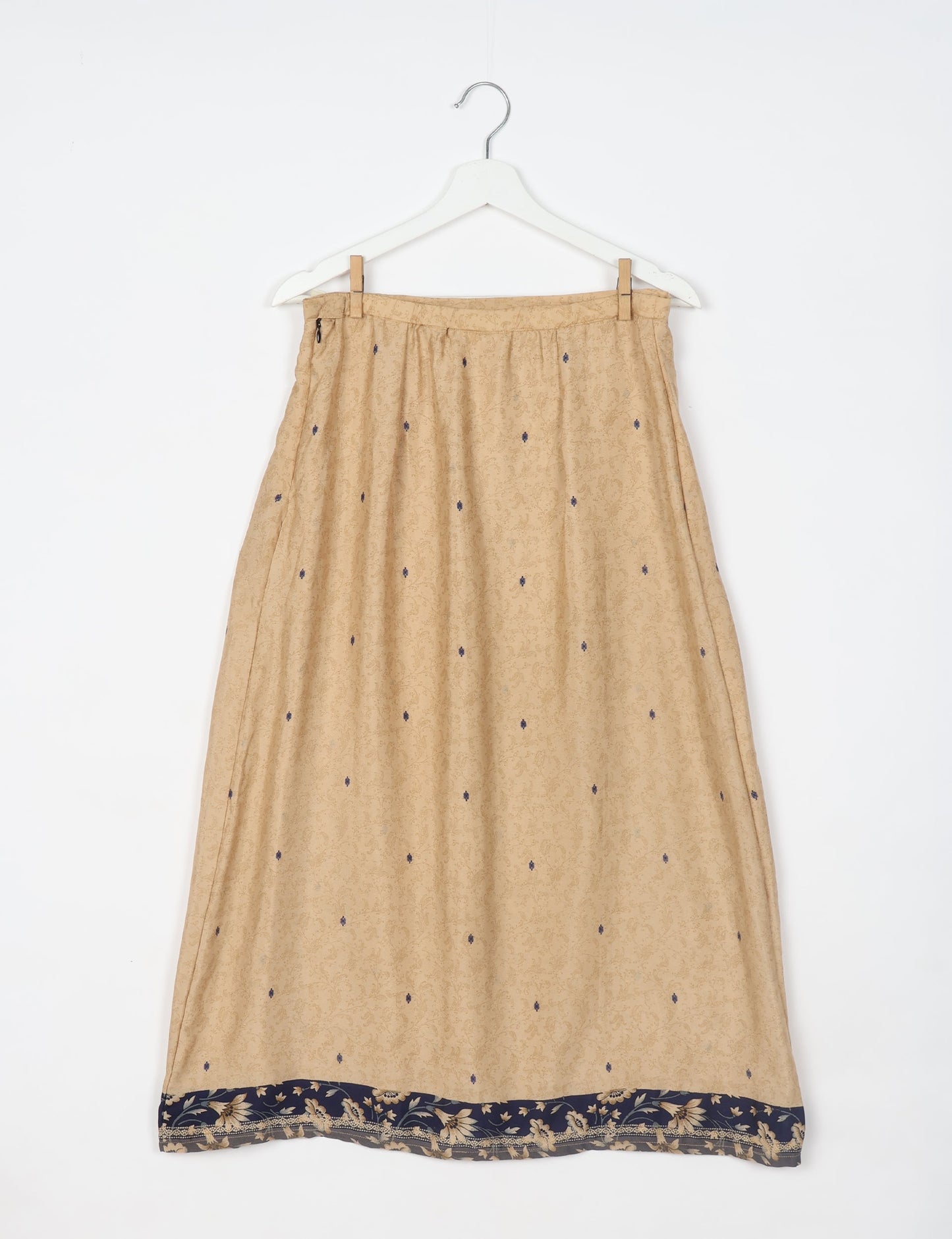 Beige A-line skirt with small dark blue dots and a dark blue floral border, hanging on a white hanger