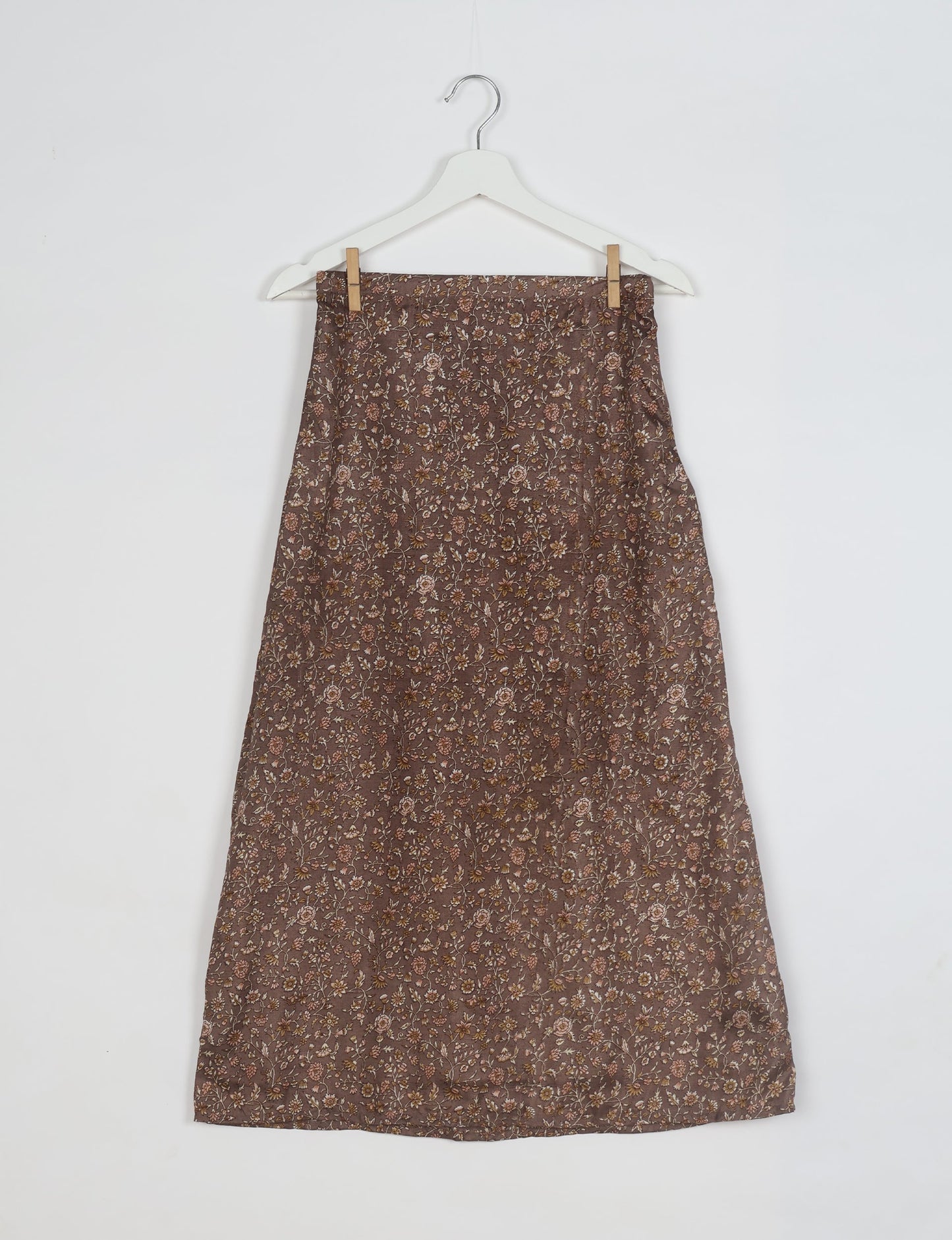 Brown A-line skirt with small floral tropical print hanging on white hanger against white background