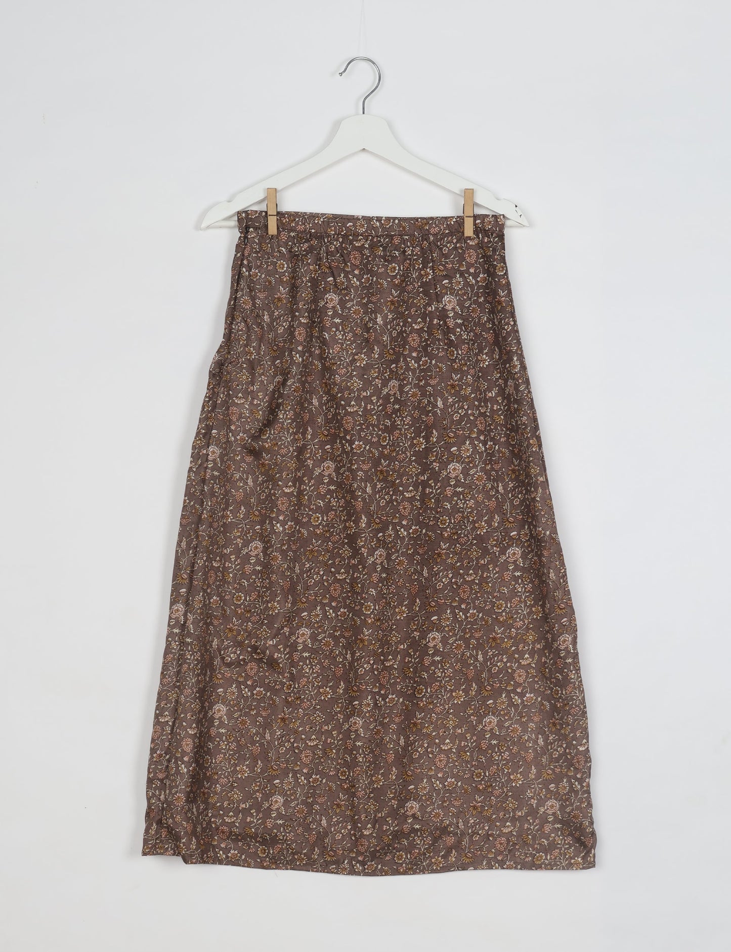 Brown A-line skirt with small floral tropical print hanging on white hanger against white background