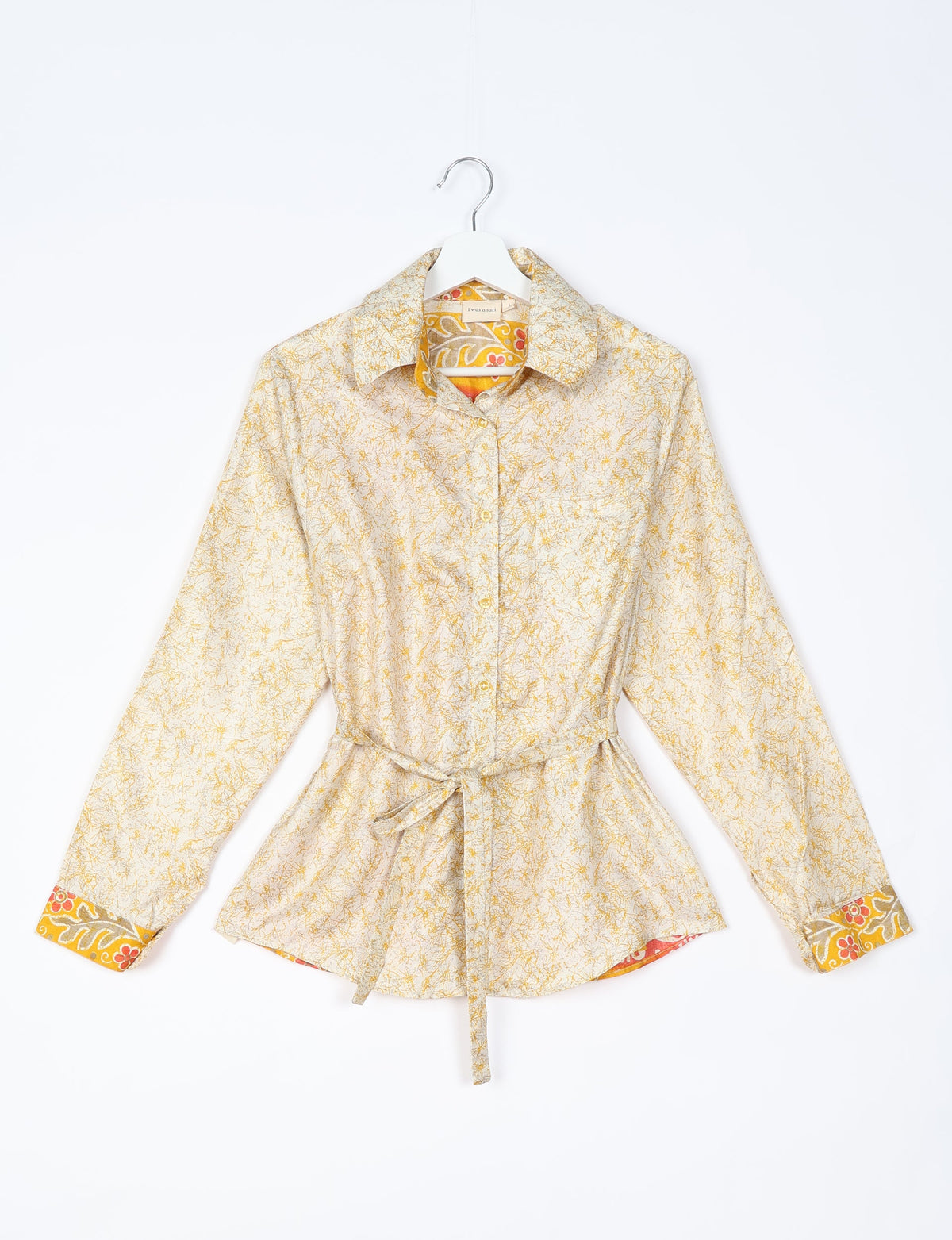 White long-sleeve button-up shirt with yellow abstract print, floral inner collar and cuffs, and waist tie, front view on hanger