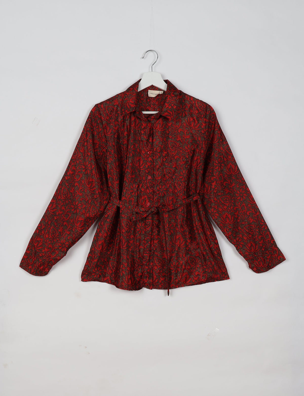 Red long-sleeve shirt with black floral pattern, button front, collar, and waist tie, hanging on white hanger