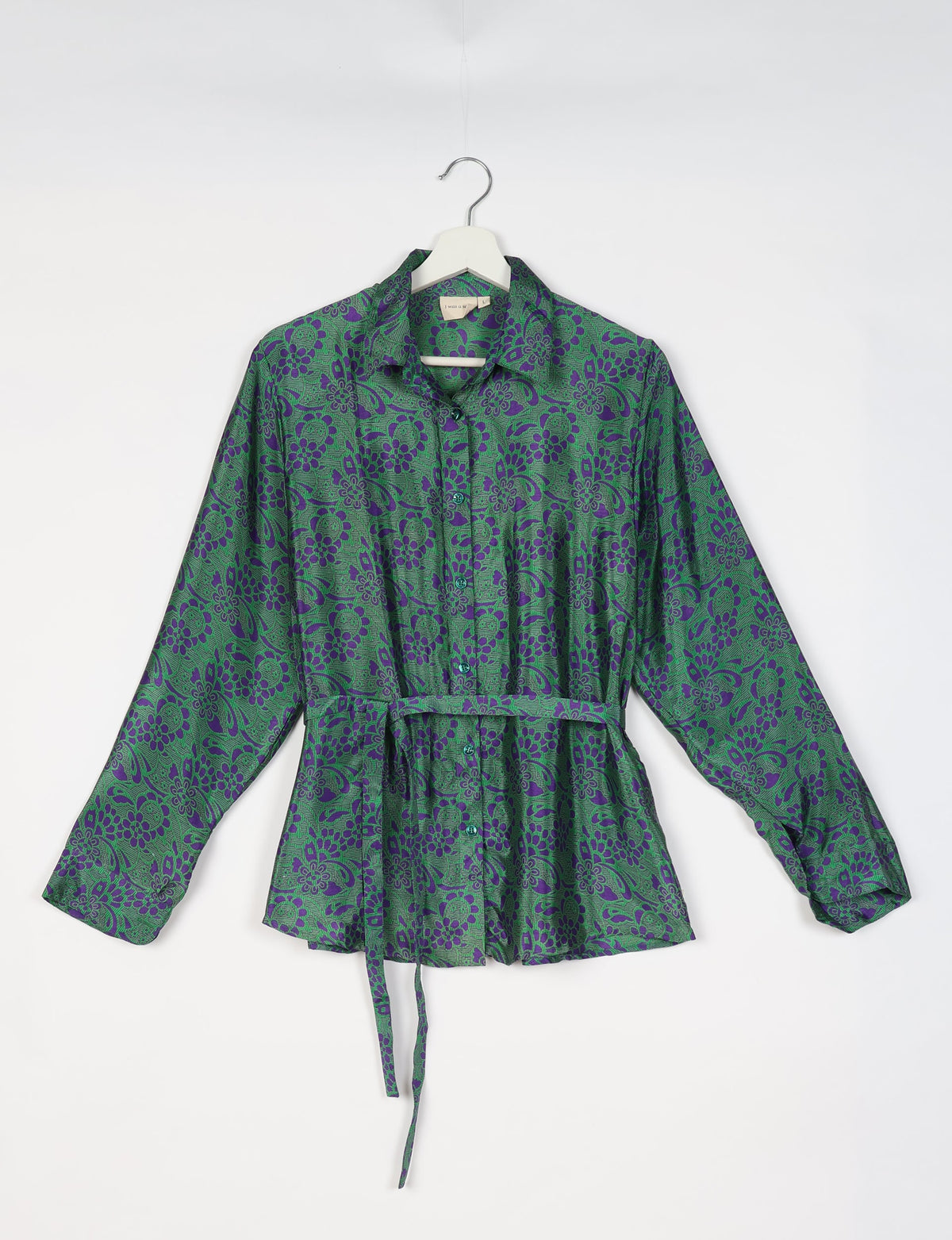 Green button-up shirt with purple floral tropical print, long sleeves, collar, and waist tie, hanging on white hanger