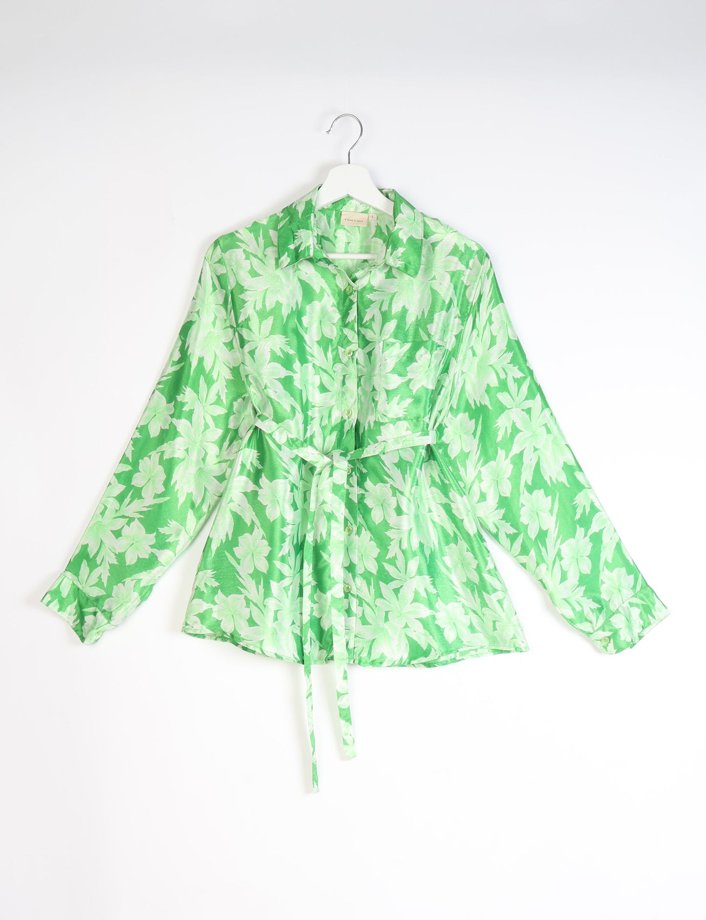 Green button-up shirt with light green leaf pattern, long sleeves, chest pocket, collar, and waist tie, hanging on white hanger