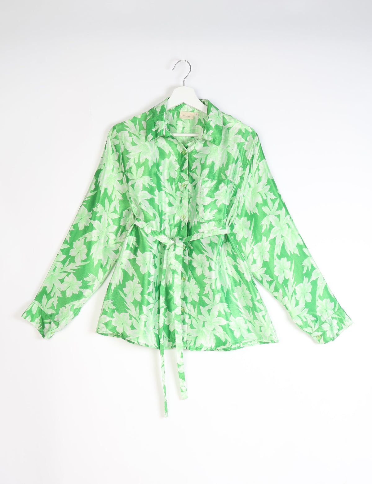 Green button-up shirt with light green leaf pattern, long sleeves, chest pocket, collar, and waist tie, hanging on white hanger